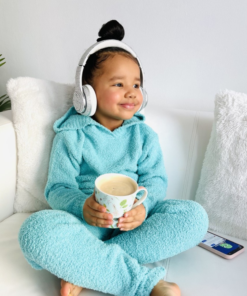 Lynnie is wearing a mint color NovaKids outfit by Fashionnova. She is sitting on the sofa smiling, listening to music and holding hot chocholate in her hands.