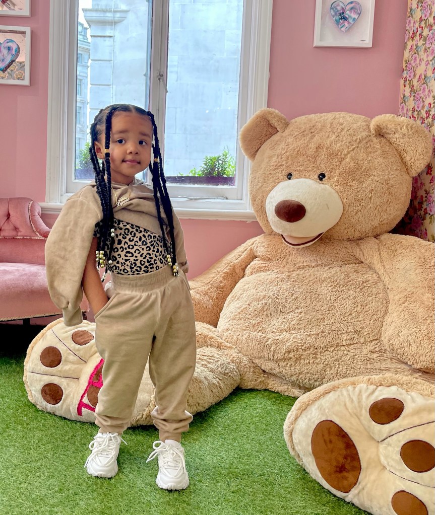 Lynnie is standing next to a giant Teddy Bear, wearing Mini Outdo Me Mineral Wash Lounge Set - Beige. 